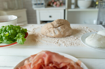 Whole wheat pizza dough on floured surface with ingredients for making a pizza
