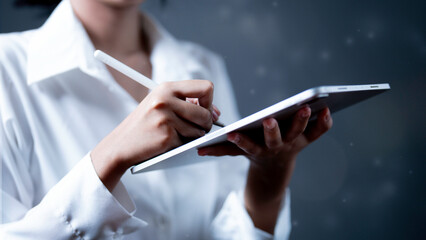 An Asian businessman holding a tablet looks at the empty space while standing against a studio background.