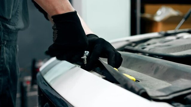 close up At a service station master auto mechanic unscrews bolts on the interior panel of a white car