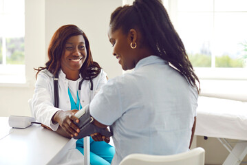 Smiling friendly african american woman doctor therapist measuring blood pressure of a young female...