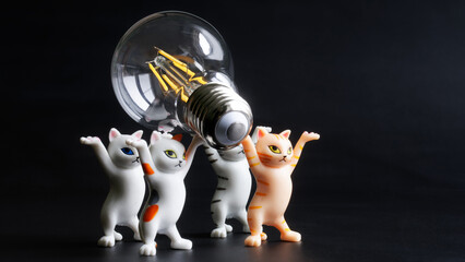 Four funny toy cats are installing a modern energy-saving LED lamp. Educational concept for...