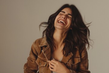 Happy woman holding her stomach and laughing out loud, chuckling giggling at amusing anecdote, sincere emotion, wearing casual style jacket. Indoor studio shot isolated on gray background