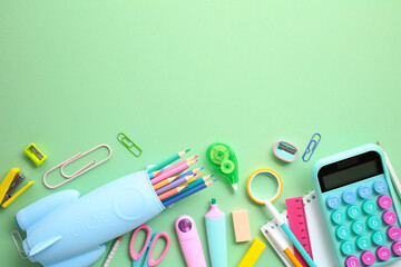 Back-to-school concept with vibrant school supplies on green background. A bright and organized display of educational tools including pencils in case, calculator, ruler, and scissors. Top view.