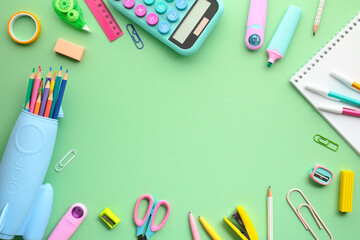 Flat lay of vibrant school or office supplies on a green background. Colored pencils in a blue case, a calculator, and various stationery items. Ideal for educational themes, back to school concept.