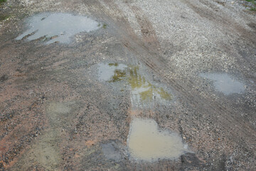 The road is wet with rainwater, has holes and is damaged.