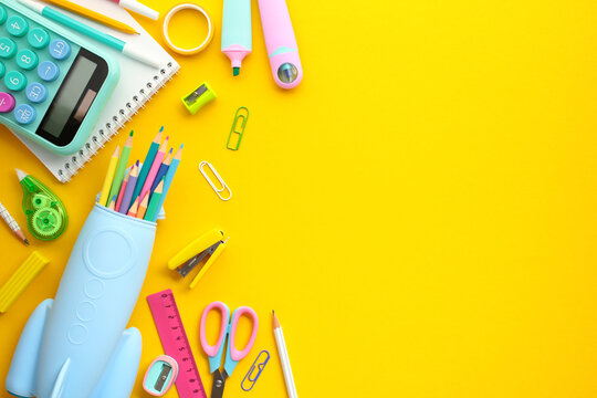 Bright Back-to-School Supplies on Yellow Background. Colorful assortment of educational tools, including calculators, colored pencils, scissors, and rulers, neatly organized on a vivid yellow surface.