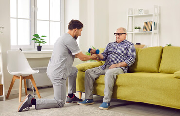 Senior man doing exercise using dumbbells with support from nurse.Young smiling caregiver...