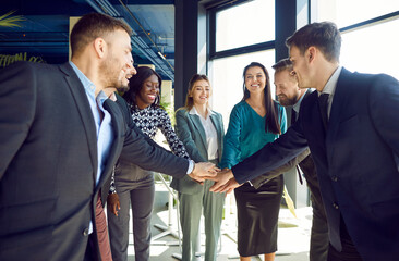 Team of happy diverse people stacking hands after business meeting. Group of multiracial men and women standing in circle in office, smiling and piling up hands. Teamwork, partnership concept