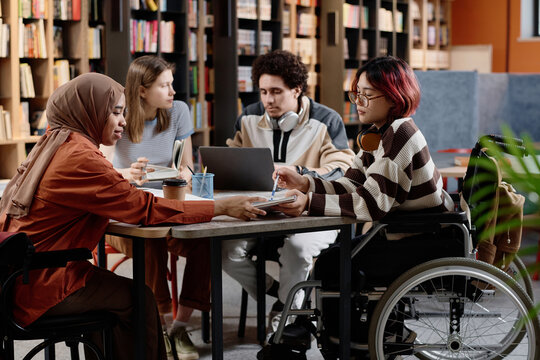 Group of diverse male and female students spending time together studying in library - Powered by Adobe