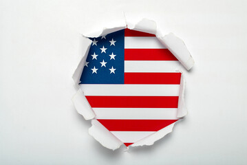 Tear hole in white paper revealing the U.S. flag underneath. American flag.