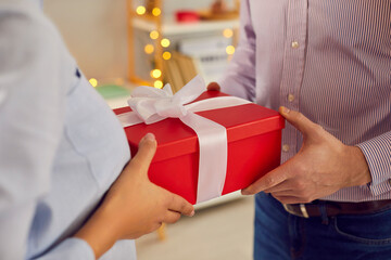 Giving present hand closeup, people in love holding red surprise gift box with ribbon, sharing...