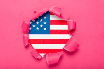 Torn hole in the dark pink paper revealing the U.S. flag underneath. Flag of the United States.