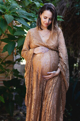 Pregnant woman smiles and touches her belly in a gorgeous lace dress