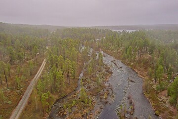 Aerial view of flowing rapids and gravel road in cloudy spring weather, Ovre Pasvik National Park, Norway.