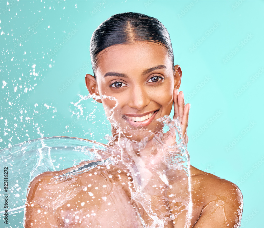 Wall mural Woman face, washing and water splash for skincare, hygiene and beauty or dermatology in studio. Indian model in portrait with liquid for natural, cosmetics and facial cleaning on blue background