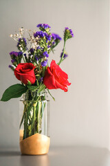 A bouquet of fresh roses with baby breath in a glass water jar on white background.
