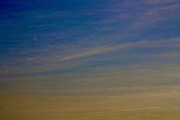 Cirrus clouds in the sunset sky. Long, smooth clouds are colored yellow-green against the blue sky during sunset.