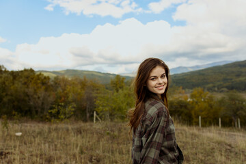 A woman in a plaid shirt enjoying the breathtaking view of mountains while standing in a picturesque field