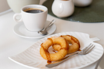 Fresh powdered sugar donuts with chocolate and cup of coffee on wooden table in cafe