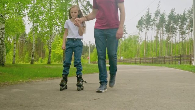 Father teach little daughter girl inline skating with roller in public park. Father's day. Happy family time together, Leisure sport activity.