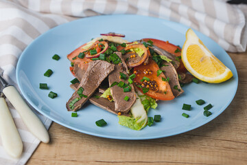 Fresh salad with pork heart, lettuce, tomato, green onion and lemon in blue plate on wooden table