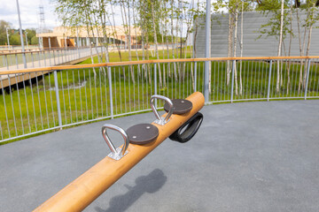 A modern playground features a wooden seesaw with safety harnesses, set against a backdrop of birch...