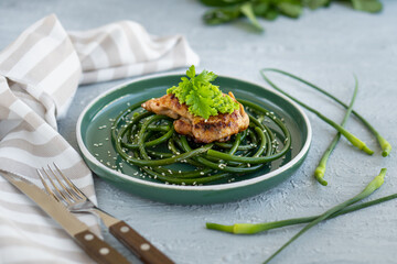 Fried chicken steak with garlic arrows and sesame seeds in green plate on gray concrete table