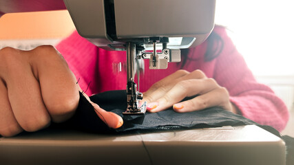 Young woman learning to sew at home with scraps of black fabric, woman with young sweater, sewing