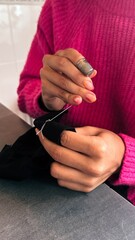 Female teen girl learning to sew by hand with needle and thimble, scrap of black fabric,pink sweater