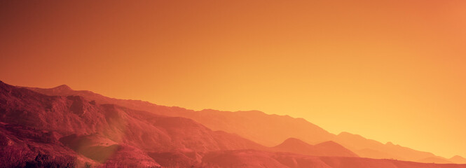 Silhouette of mountains against the orange sunset sky. Horizontal banner