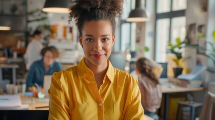 The portrait shows a Biracial Creative Young Woman working on a computer in a bright, busy office. The female manager is smiling and having a productive day while other people are working behind her.