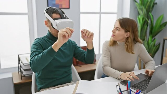 A man using vr headset with woman coworker at laptop in modern office.