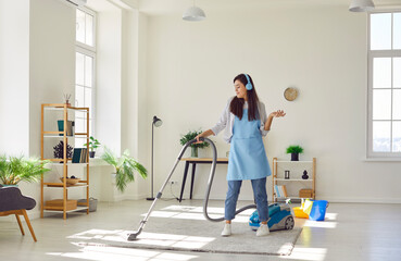 Cheerful happy cleaner, female homeowner having fun while tidying up at home, vacuuming carpet,...