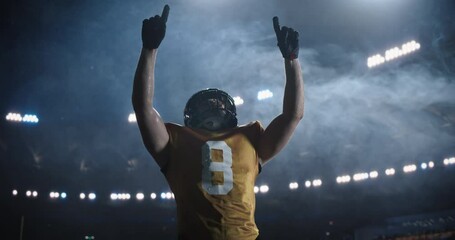 Portrait of an American Football Player Celebrating a Successful Game Victory and Raising Arms in Triumph. Male Athlete in Yellow Jersey, Helmet and Gloves Showing Confidence and Strength