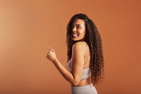 Woman in a bra looking over her shoulder and smiling on an orange background