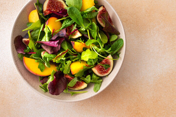 Salad with mixed lettuce and peaches with figs, plate with salad on beige background