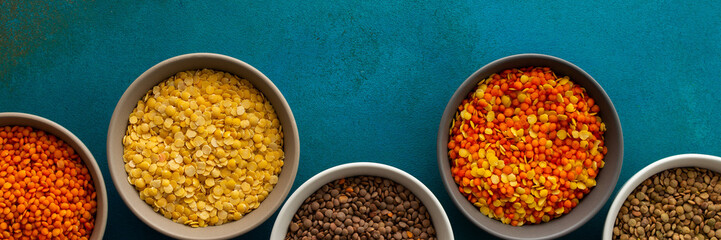 Multicolored lentils in bowls banner, yellow and brown, green and orange lentils, healthy legumes, top view, copy space