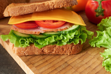 An appetizing ham, cheese and vegetable sandwich on a wooden board. Quick breakfast.