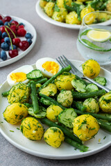 Delicious lunch or dinner, boiled young potatoes with asparagus beans and young fresh cucumbers, boiled eggs and fresh berries, refreshing water with lemon and mint