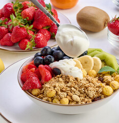 Granola with strawberries, kiwi, banana and blueberries in a round plate topped with yogurt on the table. Healthy and tasty food