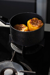 Stuffed peppers with meat and rice cooking in a pot on the stove in red tomato sauce. Sauce is bubbling and steaming, creating a delicious and appetizing food scene. 