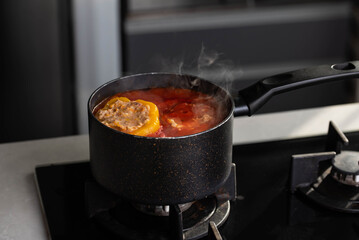 Stuffed peppers with meat and rice cooking in a pot on the stove in red tomato sauce. Sauce is bubbling and steaming, creating a delicious and appetizing food scene. 