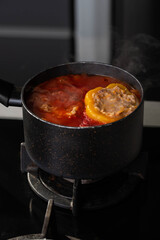 Stuffed peppers with meat and rice cooking in a pot on the stove in red tomato sauce. Sauce is bubbling and steaming, creating a delicious and appetizing food scene. 