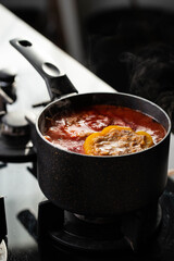 Stuffed peppers with meat and rice cooking in a pot on the stove in red tomato sauce. Sauce is bubbling and steaming, creating a delicious and appetizing food scene. 