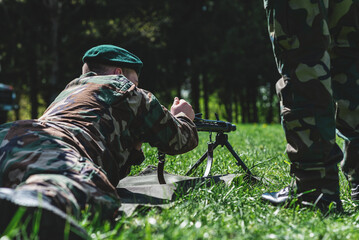 A soldier is shooting with a machine gun, a soldier is lying on the grass. Telsiai,...