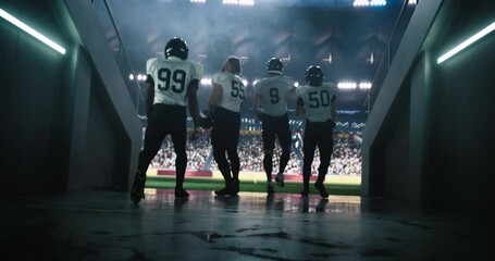 Diverse Professional American Football Team in White Uniform Walking Out of the Stadium Tunnel. Football Players are Welcomed by a Full Arena of Sports Fans in a Big Outdoors Stadium with Lights