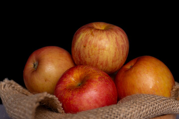 pile of red apples on a straw knitted cloth isolated black background