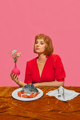 Beautiful young girl sitting at table with plate filled with seafood, fish and shrimps against pink...