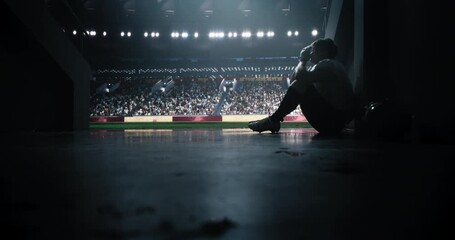 American Football Player Sitting Alone in a Stadium Tunnel, Tossing Away His Helmet. Background with a Crowded Stadium with Sport Fans. Footballer is Emotional Devastated After a Championship Game