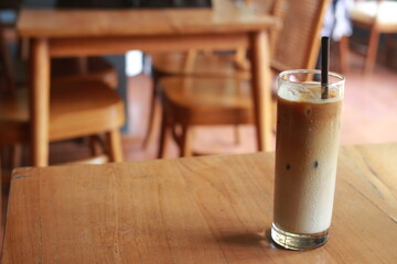 Iced milk coffee with palm sugar and straw on wooden table.